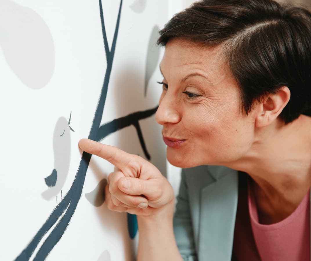 Lena Raubaum zeigt auf einen Vogel in einem illustrierten Wandgemälde.