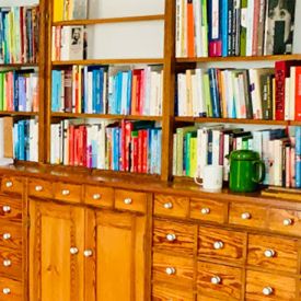 B&uuml;cherregal Heinrich beherbergt viele bunte B&uuml;cher auf seinen h&ouml;lzernen Regalbrettern. Eine Kaffekanne und ein Heferl stehen auf seinem Unterbau.