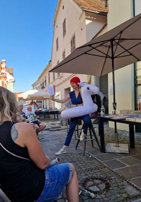 Lena Raubaum liest mit Sonnenbrille, Badehaube und Einhorn-Schwimmtier vor dem Morawa Hartberg.